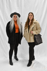 Model wearing women's black fur coat with snap buttons with another model wearing a brown button up fur coat.