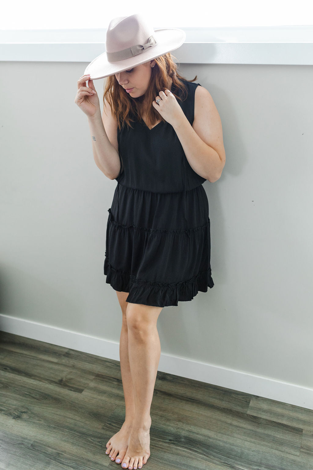 Model wearing women's little black sleeveless dress with ruffles, paired with a hat.