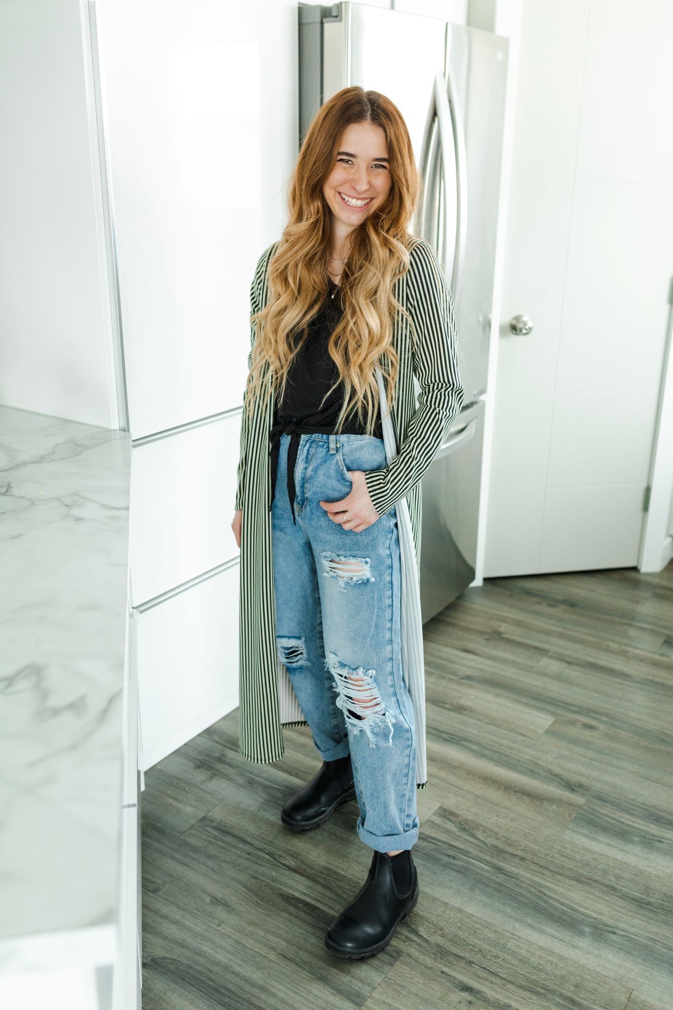 Model wearing women's light wash high waisted straight jeans with cropped bottoms, paired with long striped cardigan.