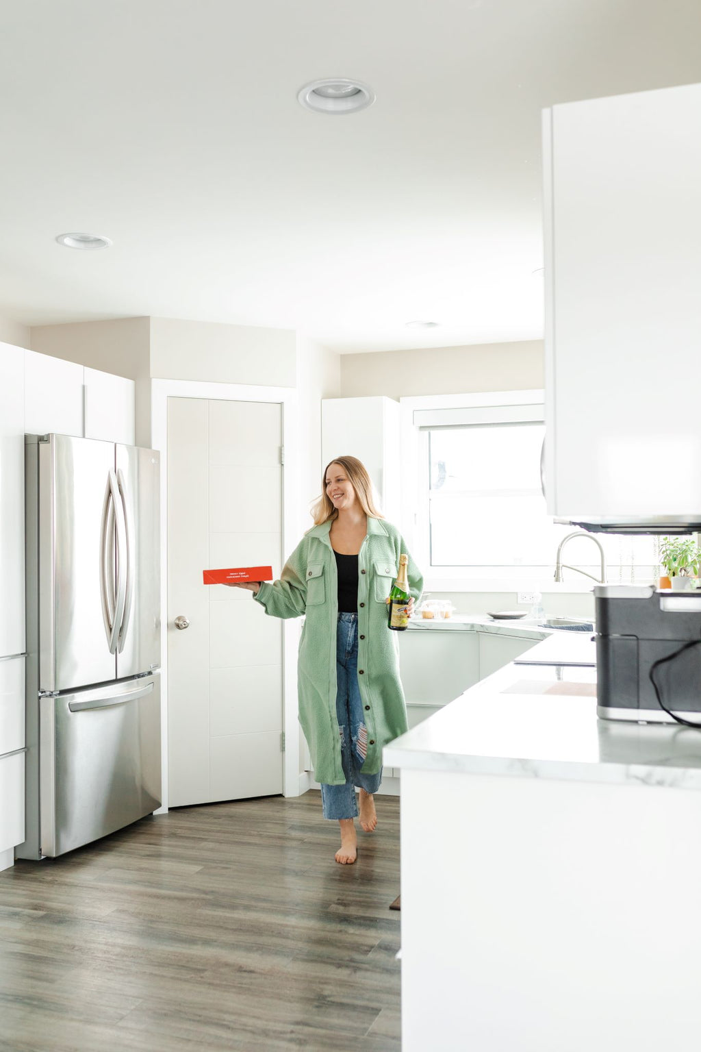 Woman at home wearing sage green long fleece jacket paired with jeans.