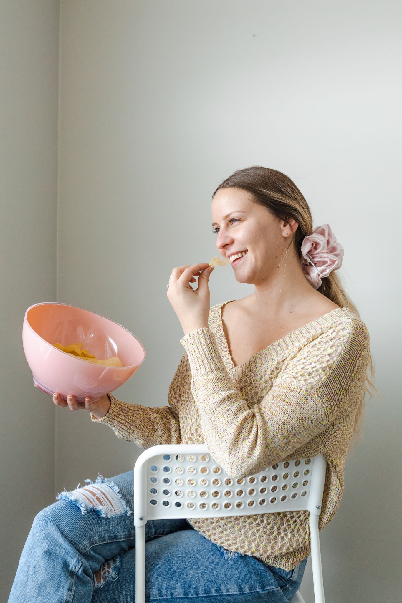 Woman enjoying a snack while wearing a tan/multicolored V-neck knit sweater.