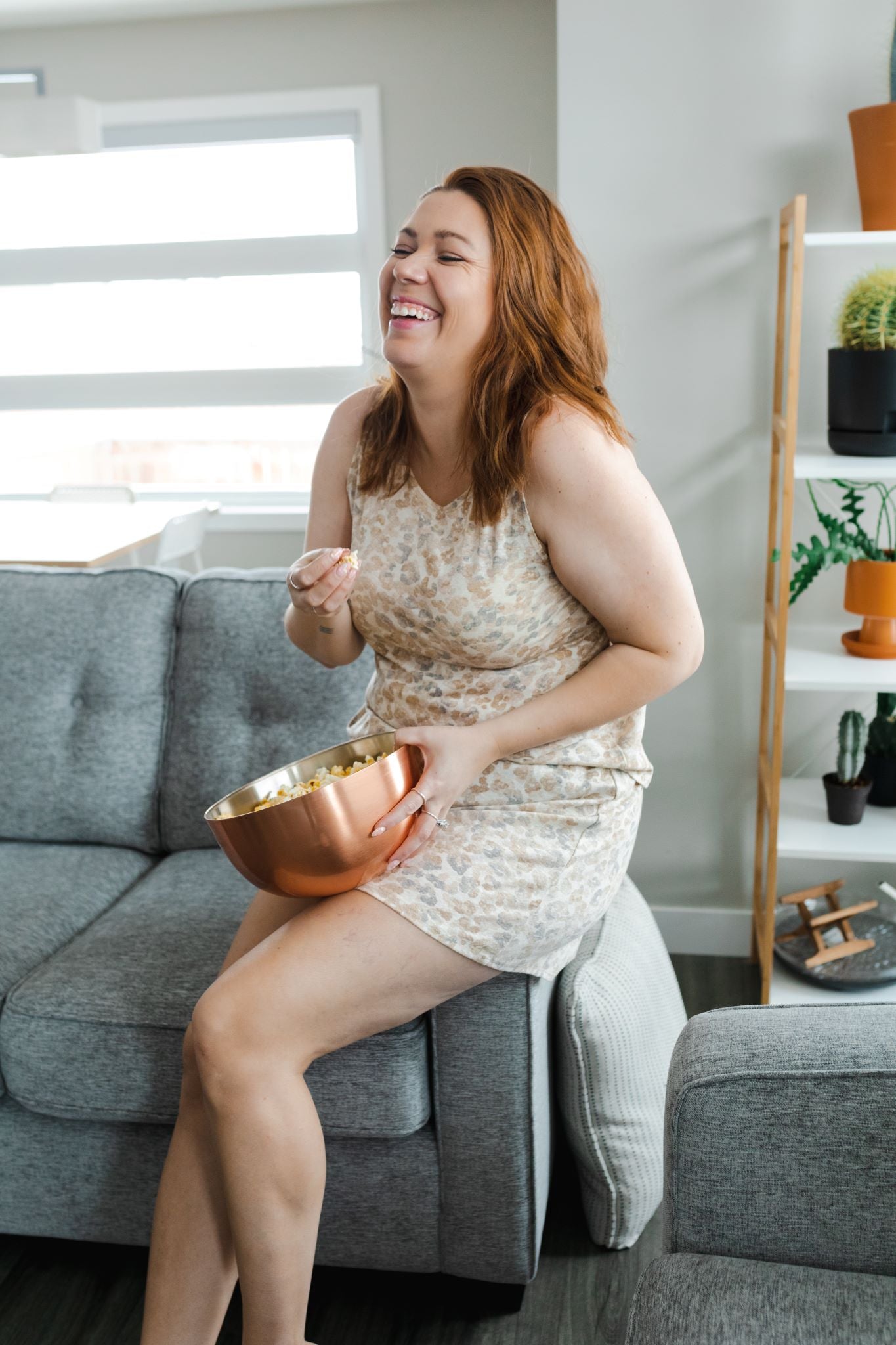 Woman relaxing on couch while wearing a tan leopard tank and shorts loungewear set.